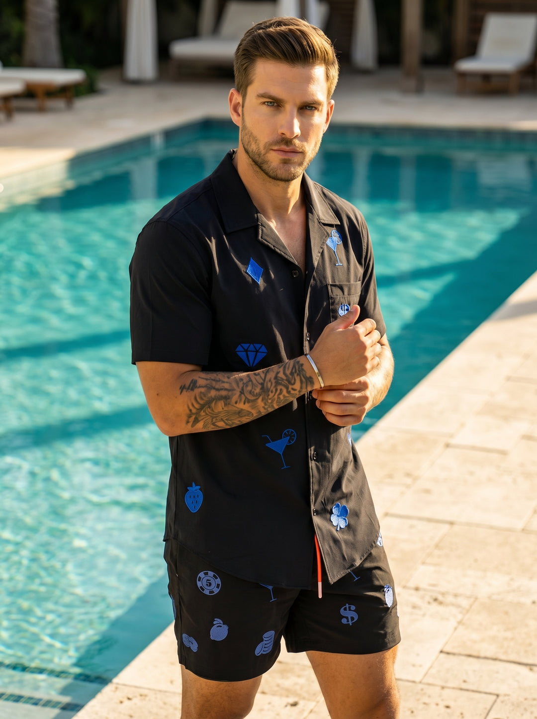 These black performance shorts feature an elastic drawstring waistband with vibrant orange cords. The fabric is decorated with blue embroidered casino and cocktail-themed motifs, including martini glasses, poker chips, and slot machine fruits, offering a 