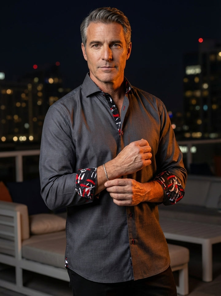 This charcoal grey long-sleeve dress shirt features a sophisticated woven texture and tailored fit. It is uniquely accented with vibrant red, black, and white abstract patterns on the inner collar and cuffs, paired with distinctive red-rimmed buttons for 