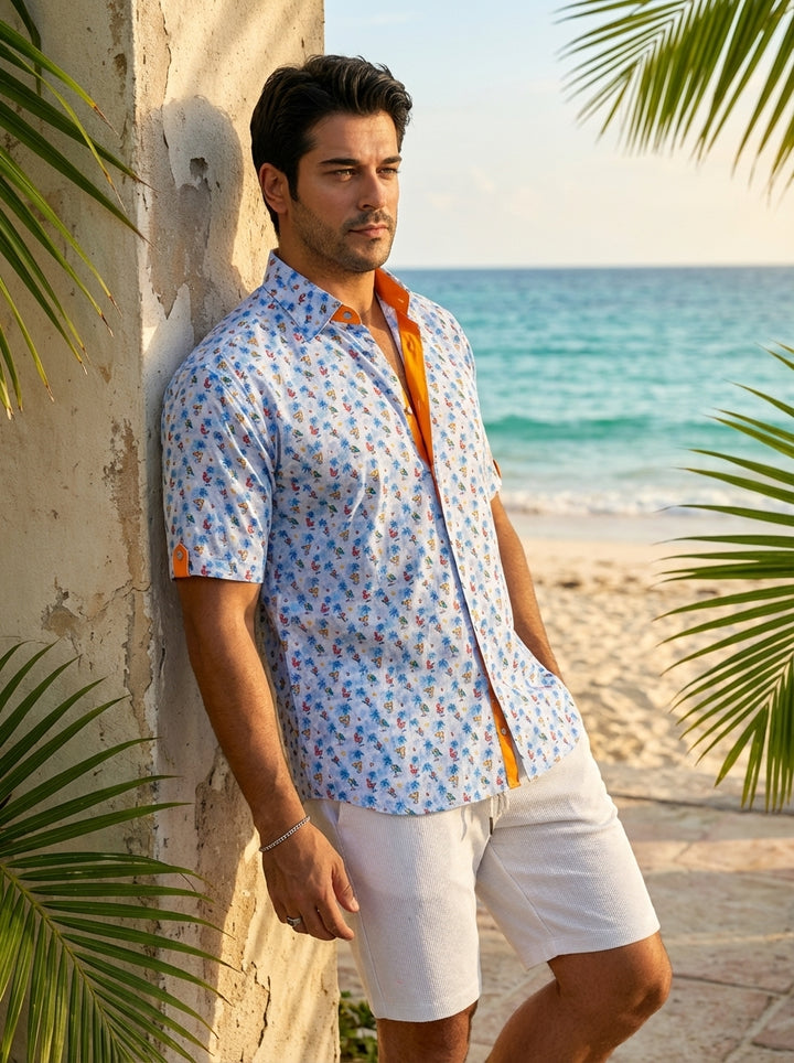 This light blue, short-sleeve button-down features a vibrant tropical print of palm trees and cocktails. Vibrant orange accents line the inner collar and sleeve tabs, adding a bold contrast to the playful summer design, perfect for warm-weather casual out