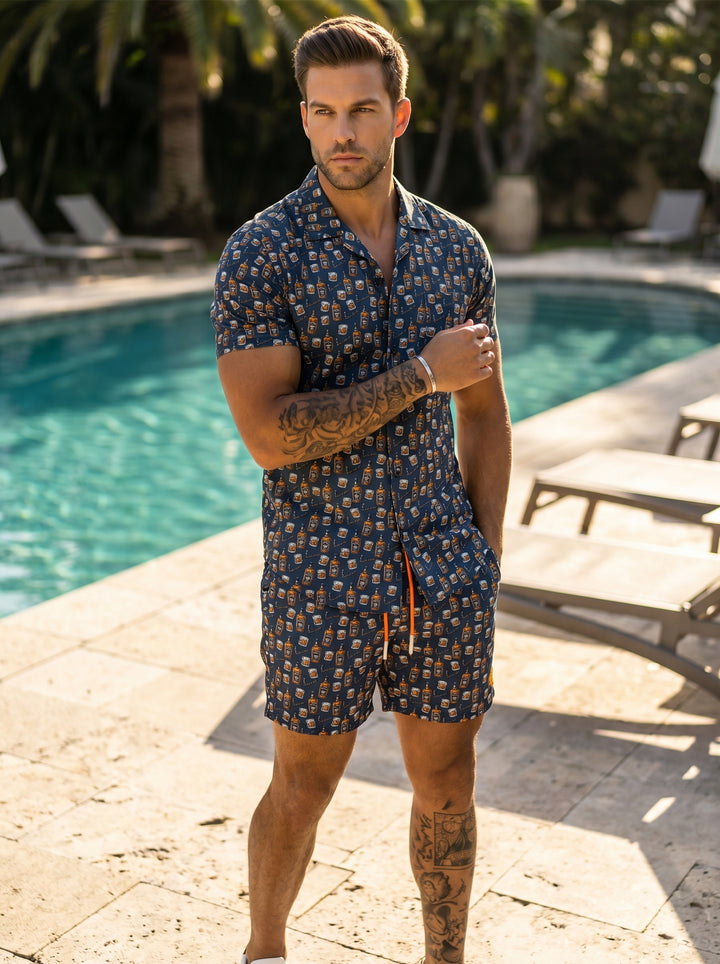 These navy blue swim trunks feature a playful all-over print of whiskey bottles and glasses. They are designed with a comfortable elastic waistband, vibrant orange drawstrings, and a mid-thigh cut, making them perfect for relaxed, stylish summer pool days