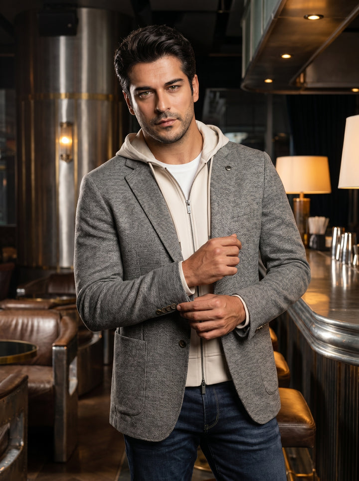 This versatile men's outfit features a textured grey two-button blazer layered over a cream-colored zip-up hoodie. The ensemble combines structured tailoring with casual knitwear, paired with dark wash denim jeans for a contemporary, smart-casual aestheti