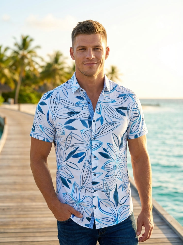 This men's short-sleeve button-down shirt features a crisp white base adorned with a vibrant blue tropical floral print. It includes a structured collar with contrast inner-placket detailing, offering a refined yet relaxed summer aesthetic perfect for cas