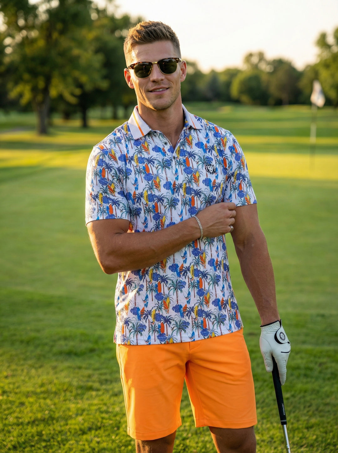 This men's short-sleeve performance polo features a vibrant tropical print with palm trees and surfboards on a crisp white base. Paired with bright orange shorts, the moisture-wicking fabric and tailored fit offer a comfortable, stylish look for warm-weat