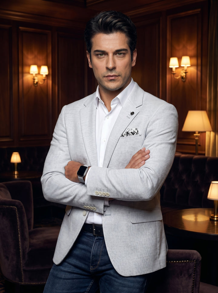 This tailored light grey blazer features a textured woven fabric, notched lapels, and a floral pocket square for a touch of elegance. Paired with a crisp white button-down and dark denim, it offers a sophisticated smart-casual aesthetic for modern men.
