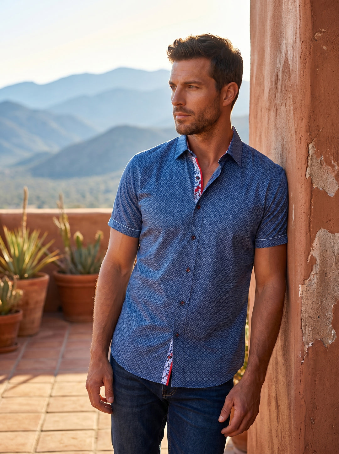A modern blue short-sleeve button-down shirt featuring an intricate diamond geometric pattern. The shirt includes a high-contrast patterned inner collar and placket with vibrant red accents, tailored for a sharp, contemporary fit that pairs perfectly with