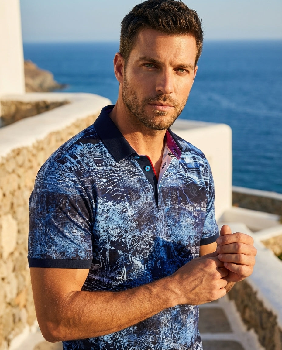 This short-sleeved polo shirt features a vibrant navy and light blue toile-inspired scenic print. It is detailed with a contrasting navy collar, bright blue buttons, and a red interior placket trim, offering a sophisticated take on classic casual menswear