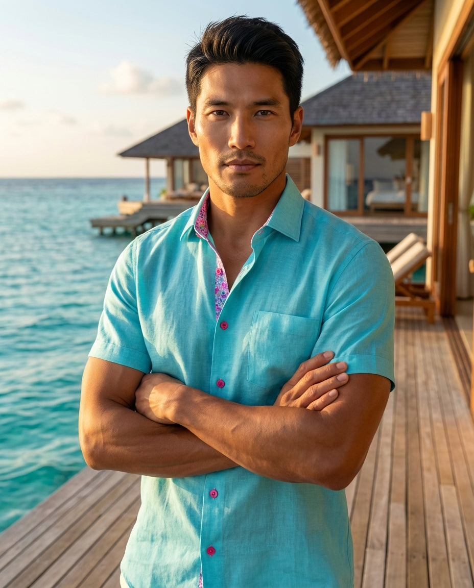 This Masutto short-sleeved linen shirt in a vibrant turquoise hue features whimsical floral contrast trim inside the collar and bright pink buttons. Its lightweight, breathable fabric makes it a sophisticated yet playful choice for warm weather style and 