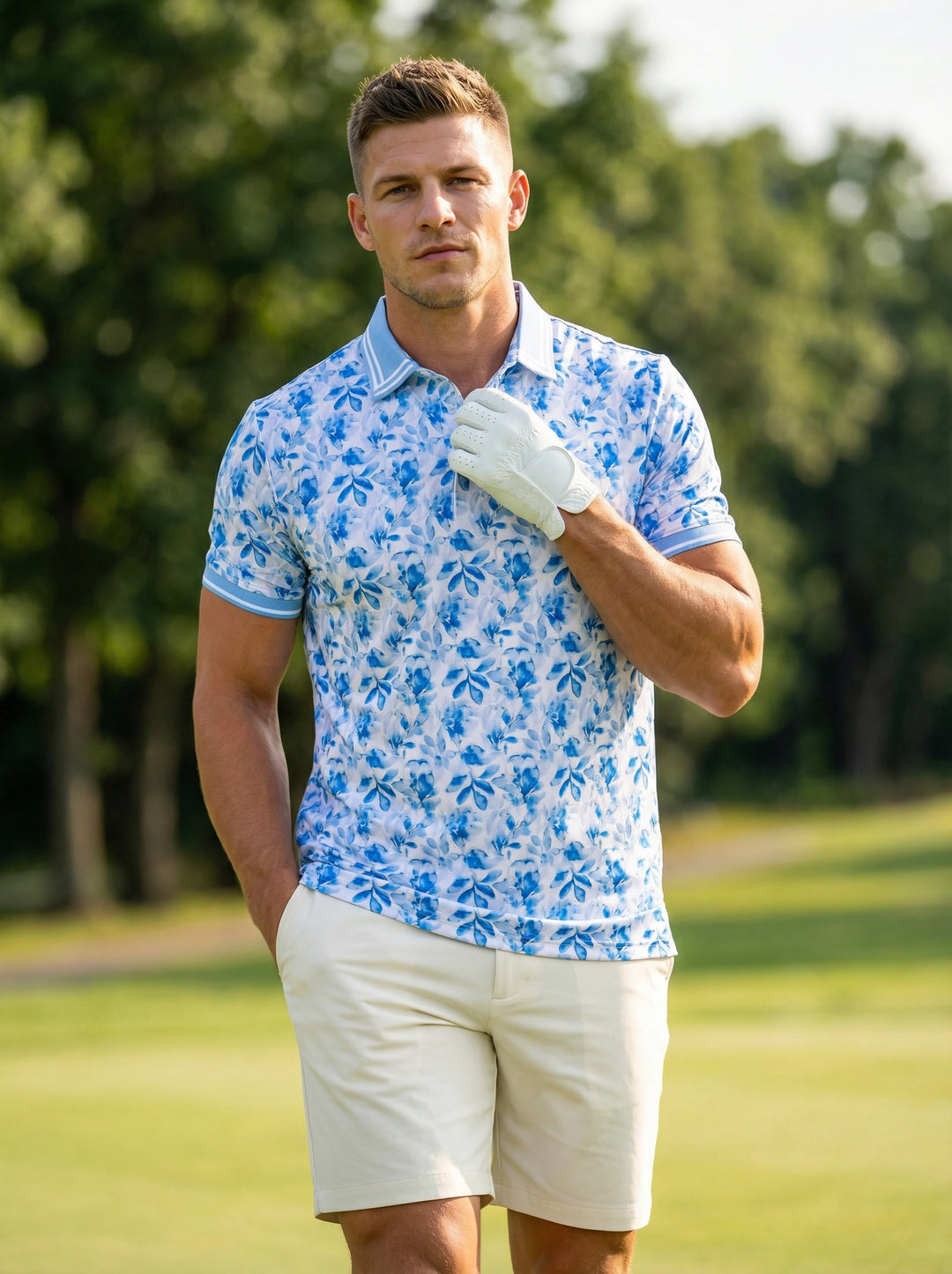 This men's performance polo features a vibrant blue and white floral-leaf watercolor print on a clean white base. It is designed with a light blue ribbed collar and sleeve cuffs, accented by white tipping for a refined, tropical look.