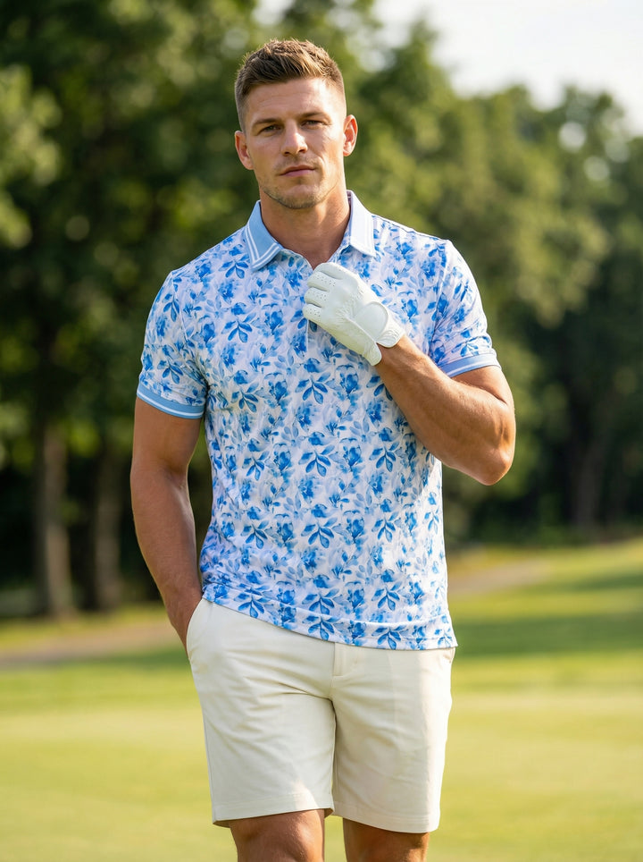 This men's performance polo features a vibrant blue and white floral-leaf watercolor print on a clean white base. It is designed with a light blue ribbed collar and sleeve cuffs, accented by white tipping for a refined, tropical look.
