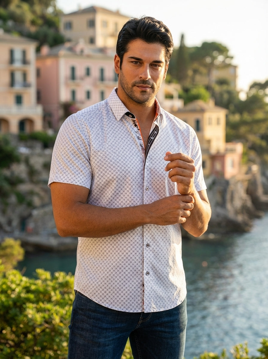 A refined men's short-sleeve button-down shirt featuring a white base with a sophisticated geometric micro-print. The design includes contrasting orange interior collar detailing and decorative buttons, paired with dark wash denim for a modern, polished s