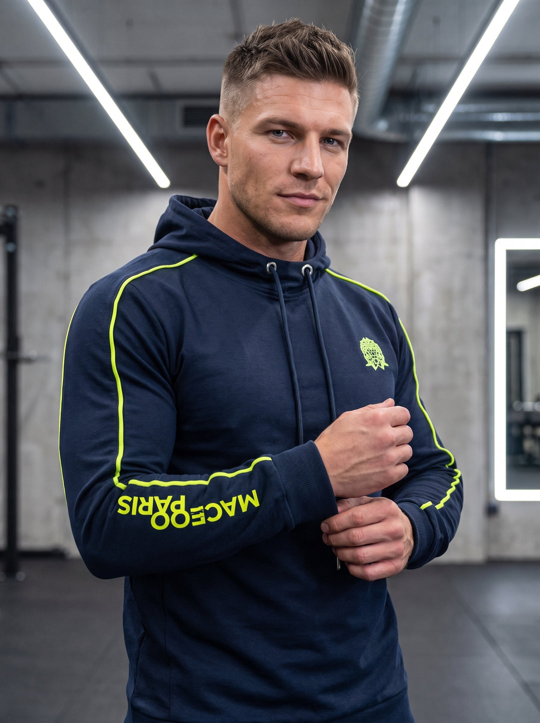 This navy blue performance hoodie features vibrant neon yellow piping along the raglan sleeves and a matching graphic crest on the chest. Crafted from a flexible, moisture-wicking fabric, it includes a drawstring hood and branded sleeve text for athletic 