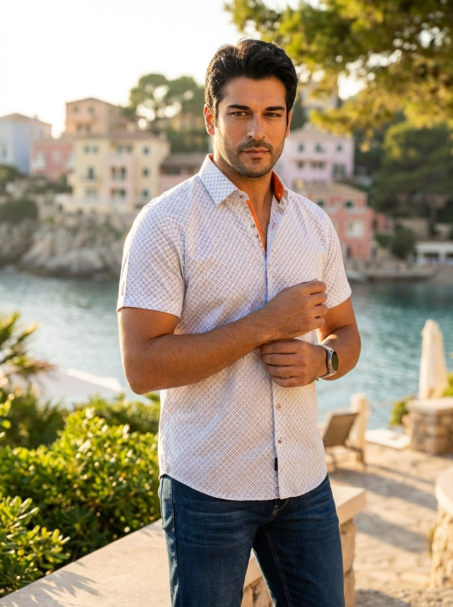 A refined men's short-sleeve button-down shirt featuring a white base with a sophisticated geometric micro-print. The design includes contrasting orange interior collar detailing and decorative buttons, paired with dark wash denim for a modern, polished s
