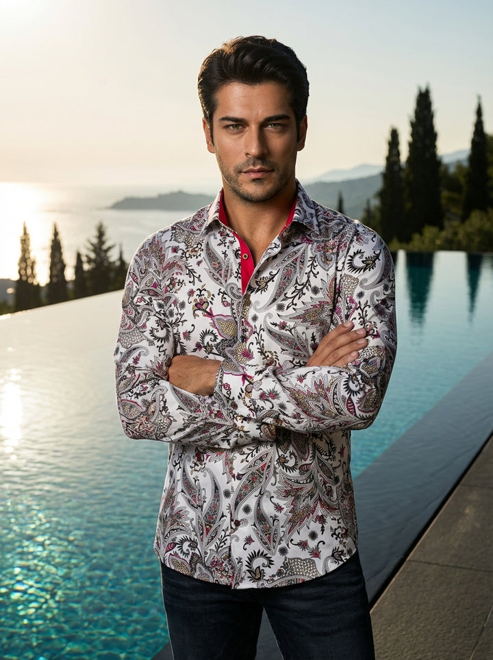 This men's long-sleeve button-down shirt features an intricate, oversized paisley print in a sophisticated palette of black, magenta, and gold on a crisp white ground. It is designed with a modern tailored fit and accented with a contrasting red inner col