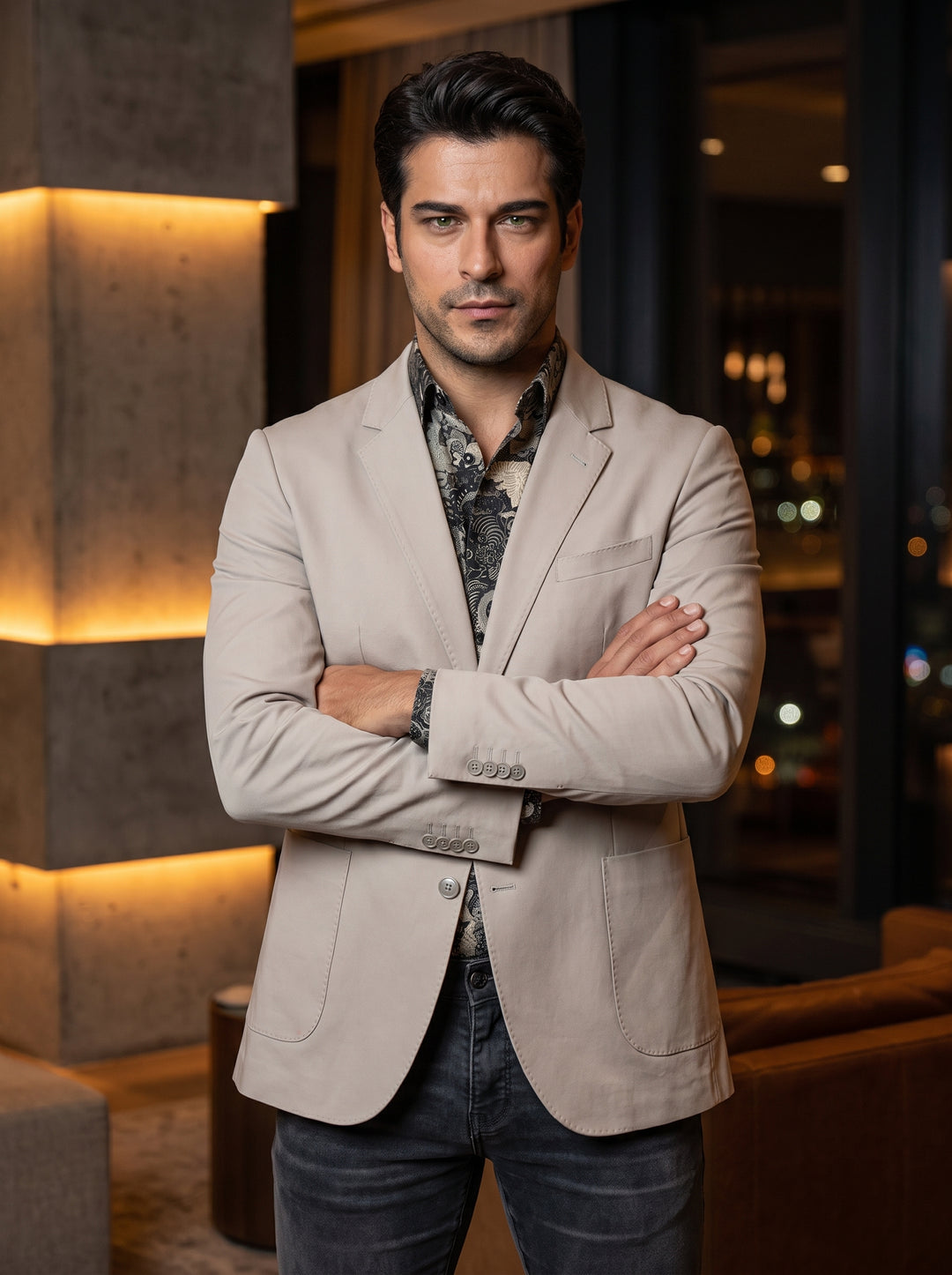 This light beige, slim-fit blazer features a notched lapel, two-button closure, and patch pockets for a relaxed take on tailoring. Styled over a dark intricate patterned shirt and denim, it offers a sophisticated yet effortless aesthetic for modern men.