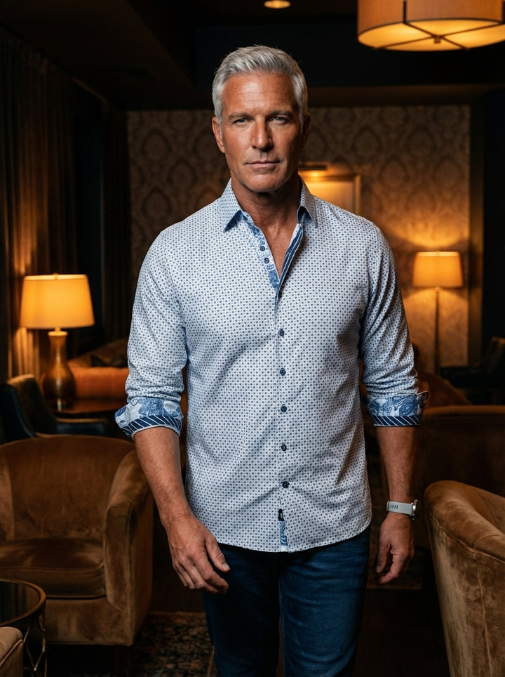 This sophisticated light blue button-down shirt features an intricate navy geometric micro-dot pattern. The design is elevated by striking contrast floral and paisley prints on the inner collar and rolled cuffs, offering a modern twist on classic men's ta