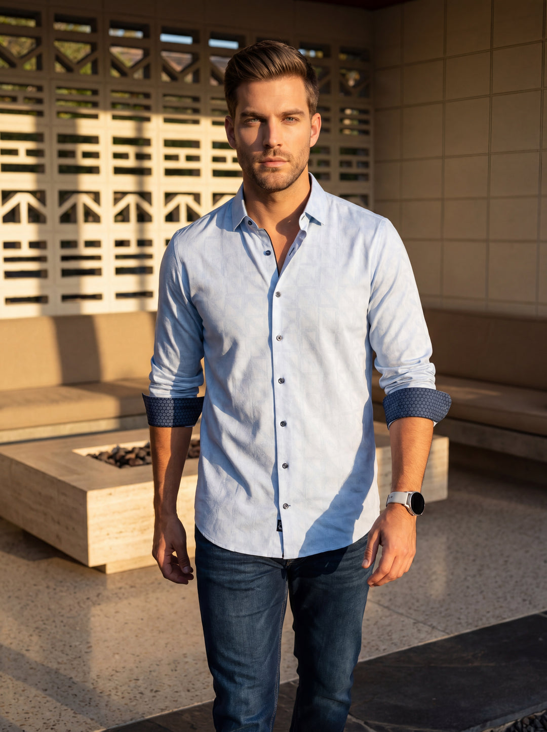 This light blue button-down shirt features a subtle geometric jacquard pattern. It includes contrasting dark blue patterned lining on the cuffs and inner collar, dark buttons, and a tailored fit, paired here with dark denim and a modern smartwatch.