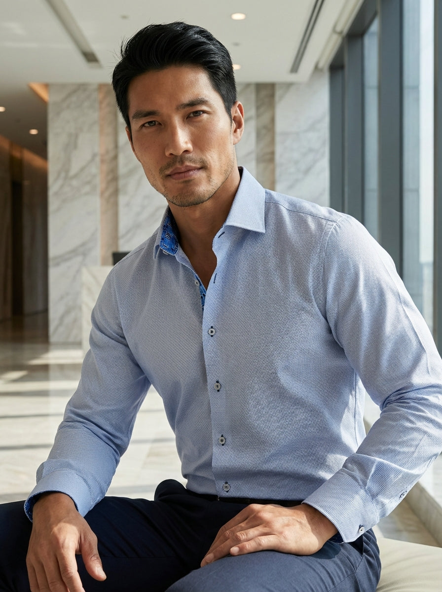 This Masutto long-sleeve button-up features a sophisticated light blue micro-patterned weave. Crafted for elegance, it includes contrast geometric patterned trim inside the collar and cuffs, complemented by distinctive dark cross-stitched buttons for a po