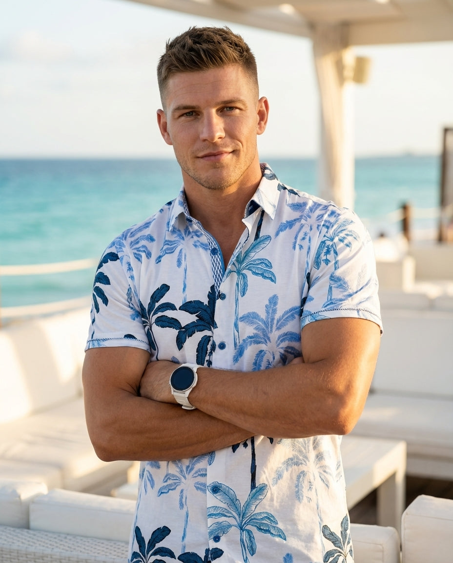 This stylish white short-sleeve button-down shirt features a vibrant blue palm tree pattern, perfect for tropical vibes. Crafted with a crisp collar and intricate inner placket detailing, it offers a refined yet relaxed aesthetic suitable for warm weather