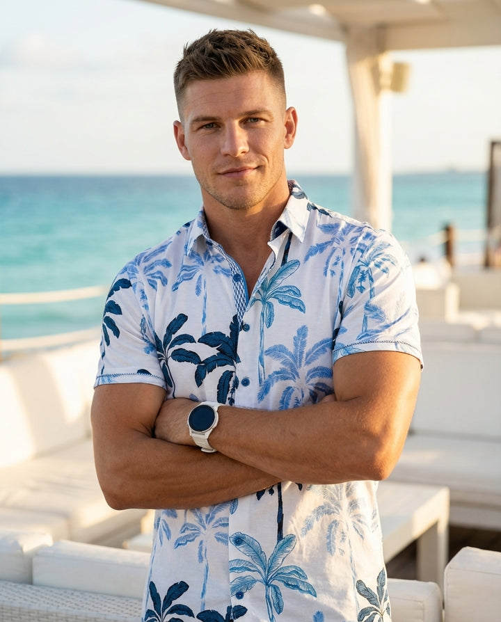 This stylish white short-sleeve button-down shirt features a vibrant blue palm tree pattern, perfect for tropical vibes. Crafted with a crisp collar and intricate inner placket detailing, it offers a refined yet relaxed aesthetic suitable for warm weather