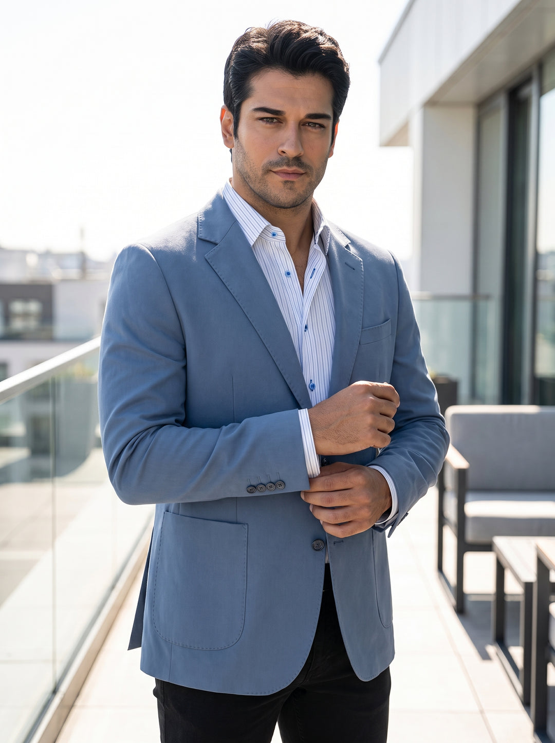 This tailored dusty blue blazer features a slim fit, notch lapels, and functional patch pockets for a contemporary smart-casual look. It is layered over a crisp pinstriped button-down shirt with blue accents, offering a sophisticated yet relaxed aesthetic