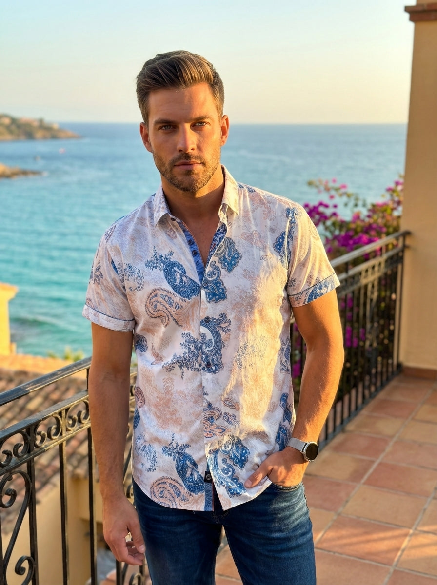 This men's short-sleeve button-down shirt features a vibrant blue and peach paisley motif on a crisp white background. Crafted with a classic collar and contrasting inner placket details, it offers a sophisticated yet relaxed aesthetic for versatile warm-