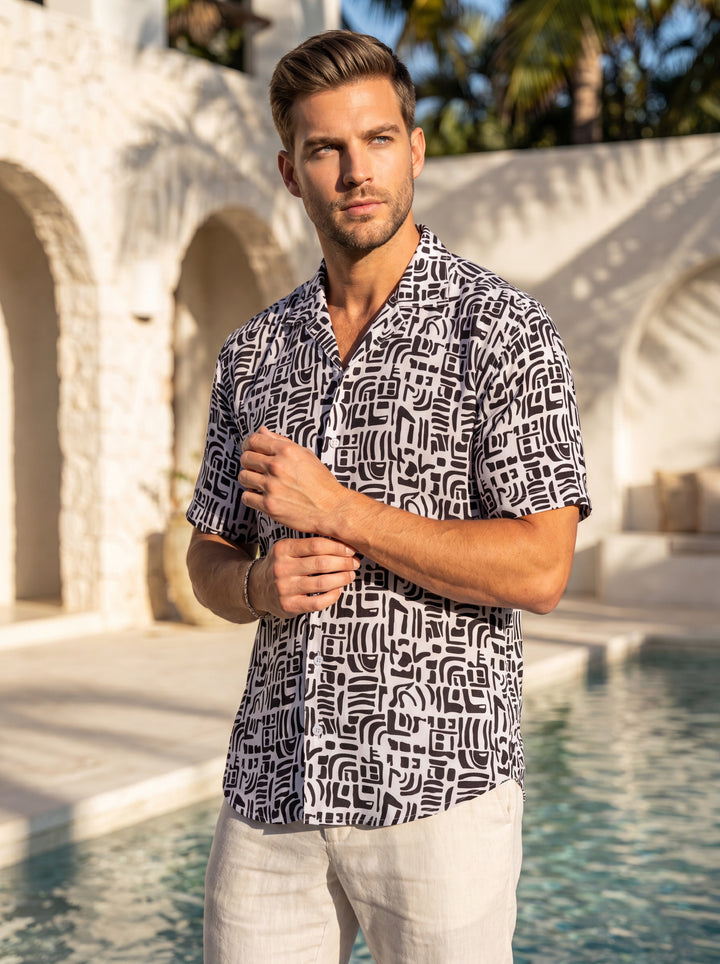 This men's short-sleeve button-down shirt features a bold, monochromatic tribal-inspired geometric print. Crafted from a lightweight, breathable fabric with a relaxed camp collar and white buttons, it offers a contemporary and artistic look perfect for wa