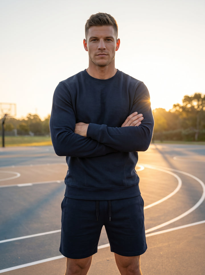 This premium navy blue coordinate set features a long-sleeve textured crewneck sweatshirt with ribbed cuffs and matching drawstring shorts. Crafted for comfort and versatility, the ensemble offers a tailored athletic fit suitable for lounge wear or modera