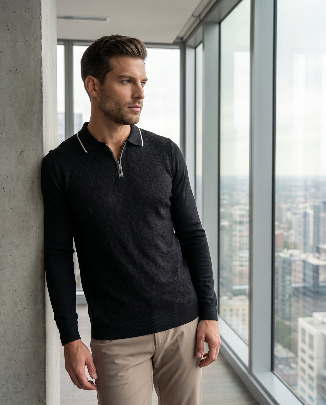 This sophisticated black long-sleeved polo features an intricate textured diamond knit pattern across the torso. It is designed with a sleek quarter-zip neckline and contrasting white tipping on the collar for a modern, refined look that blends comfort an