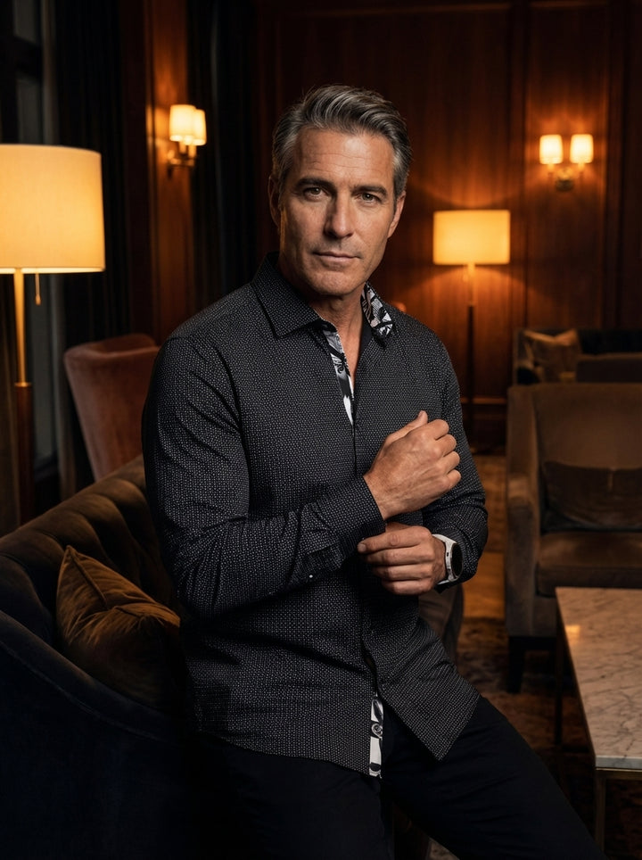 This sophisticated men's button-down shirt features a fine white micro-dot pattern on a crisp black base. Its modern design includes a contrasting graphic print lining on the collar and placket, offering a sharp look for upscale social events or evenings.
