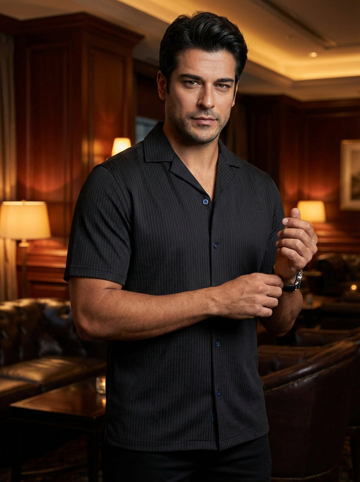 This sophisticated black short-sleeve button-down features a subtle textured pinstripe pattern and a classic camp collar. Crafted for a modern fit, it includes contrasting blue buttons and interior stitching details, perfect for a refined yet relaxed even