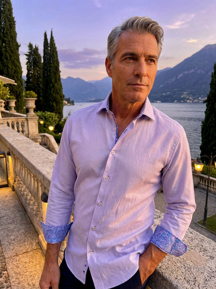This Masutto men's dress shirt features a sophisticated light lavender hue with a subtle textured weave. It boasts elegant contrasting paisley trim inside the collar and cuffs, complemented by purple-stitched buttons for a refined, modern aesthetic suitab
