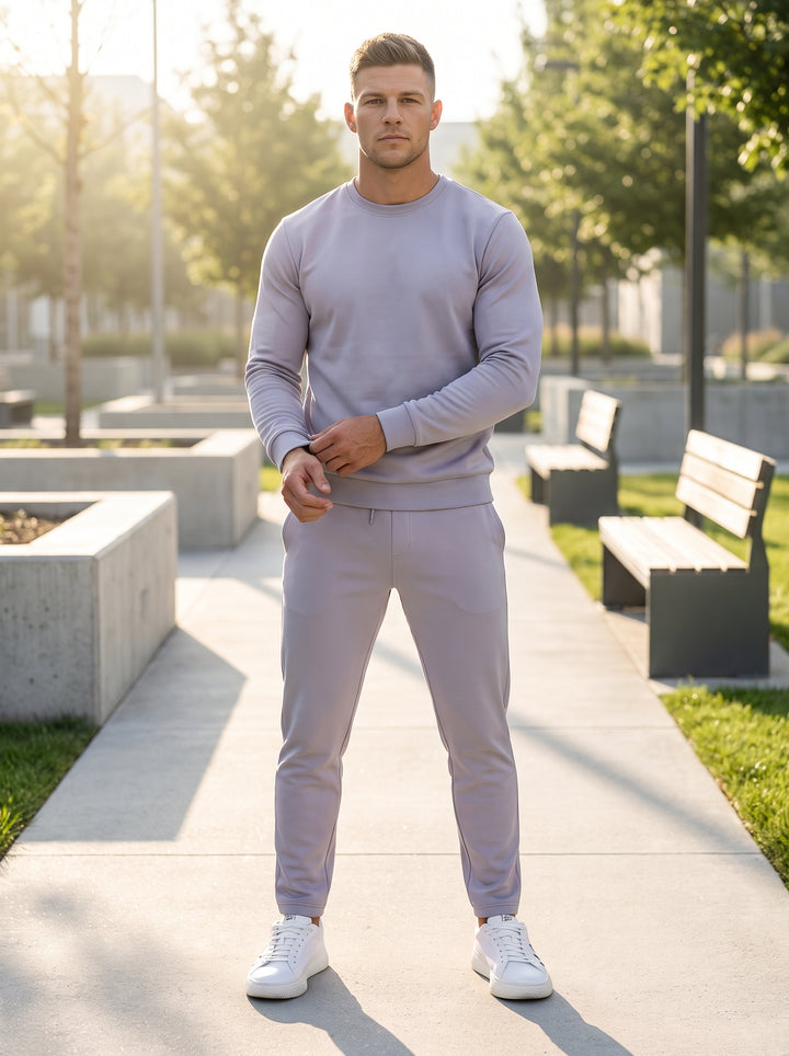 These modern men's slim-fit joggers feature a clean lavender-grey hue with a technical jersey finish. Designed for versatility, they include a smooth waistband, subtle side pockets, and tapered ankles, paired here with a matching crewneck sweatshirt for a