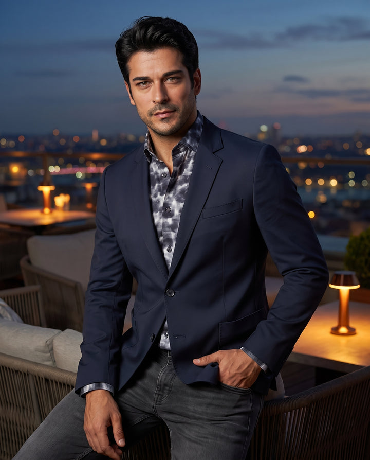 This tailored navy blazer features a modern slim-fit silhouette with notch lapels and two-button closure. Crafted from a refined matte fabric, it includes oversized patch pockets and is styled over a charcoal tie-dye print shirt for a sophisticated look.