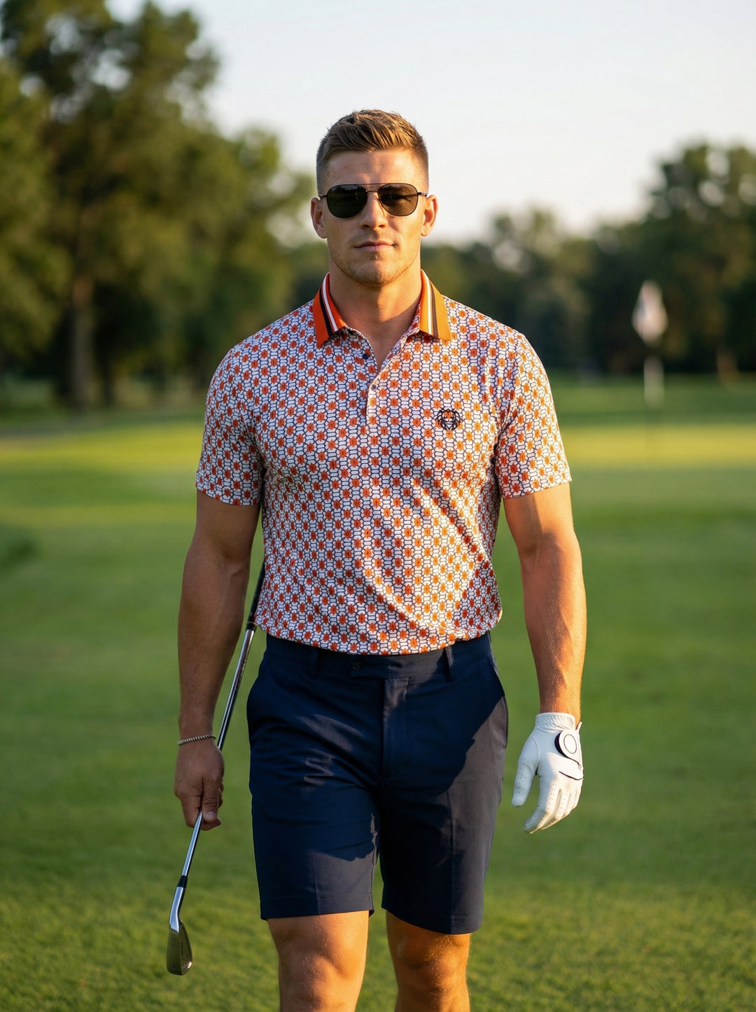 This men's short-sleeve polo shirt features a vibrant geometric link pattern in orange and white. It is accented by a bold orange collar with navy stripes, a two-button placket, and a distinct chest logo for a sophisticated athletic look.