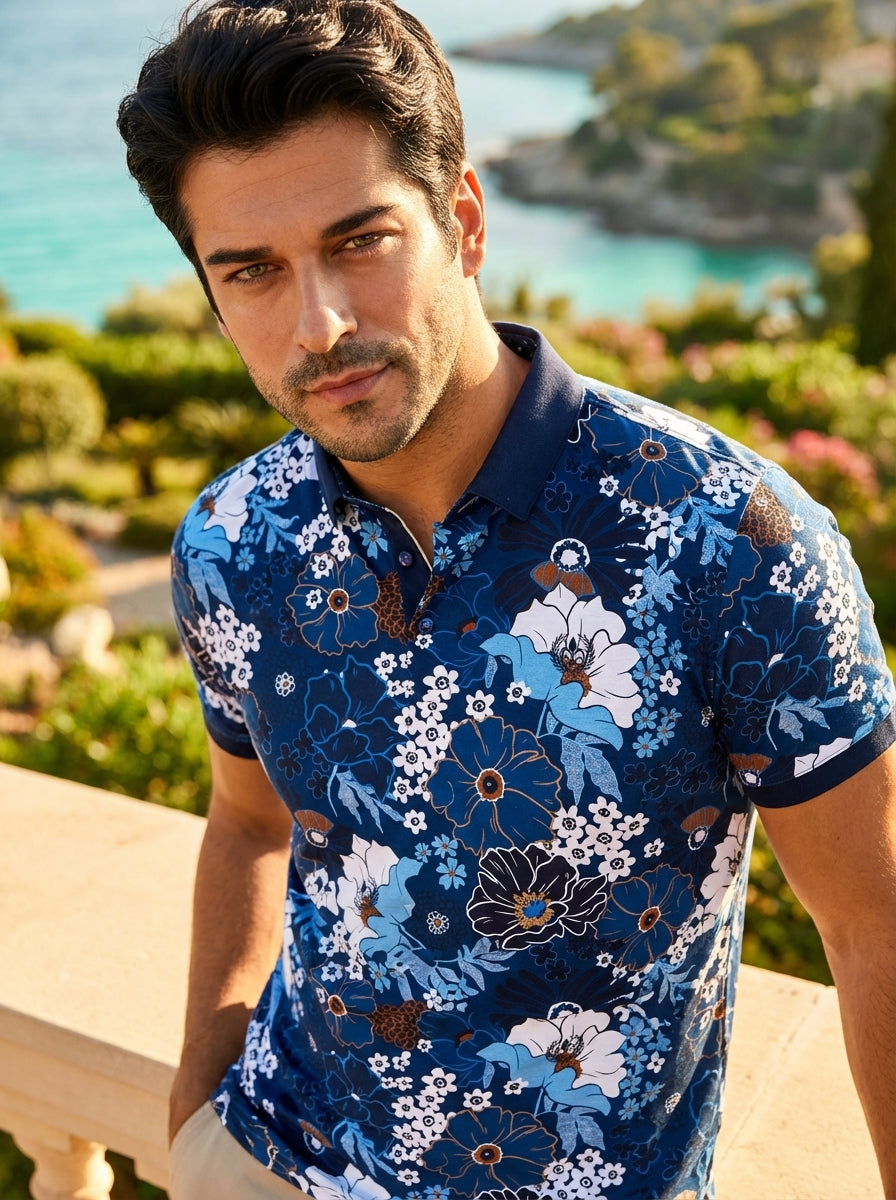 This vibrant men's polo shirt features an intricate botanical print in varying shades of blue, white, and copper. Crafted from a textured fabric, it includes a solid navy spread collar and polished buttons, blending bold floral patterns with a structured 