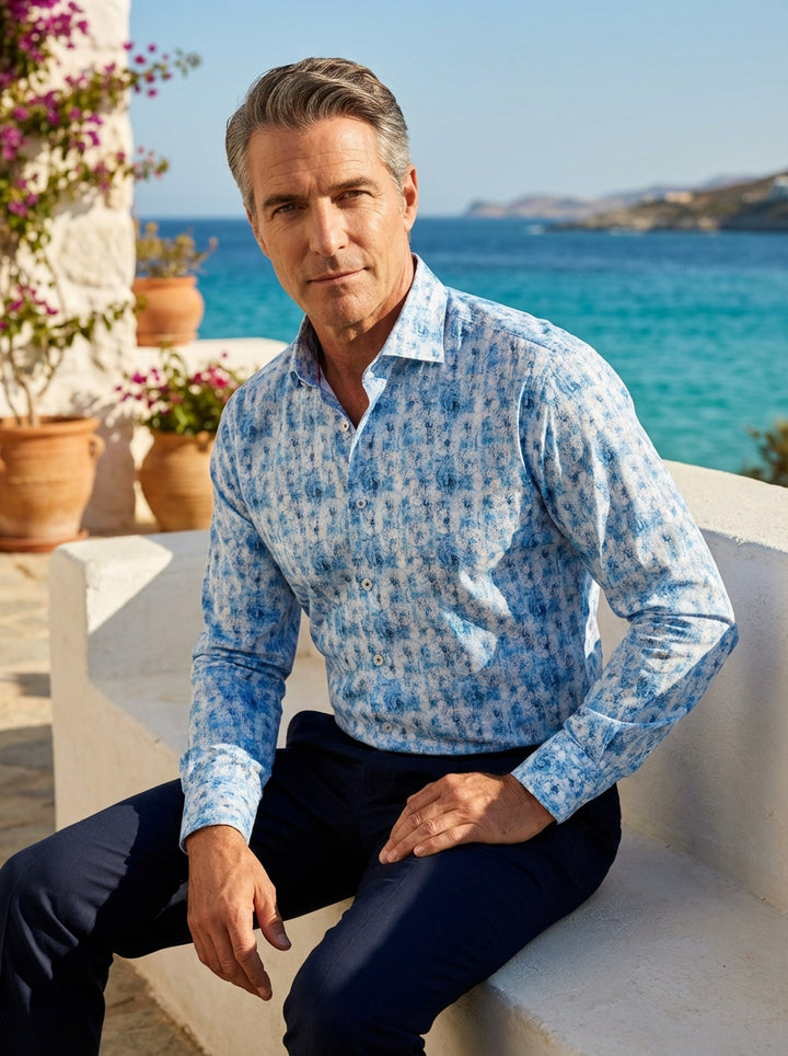This Masutto men's dress shirt features a vibrant blue and white concentric swirl print, reminiscent of ocean waves or tie-dye art. Crafted with a classic spread collar, button-down front, and adjustable cuffs, it offers a sophisticated yet energetic summ
