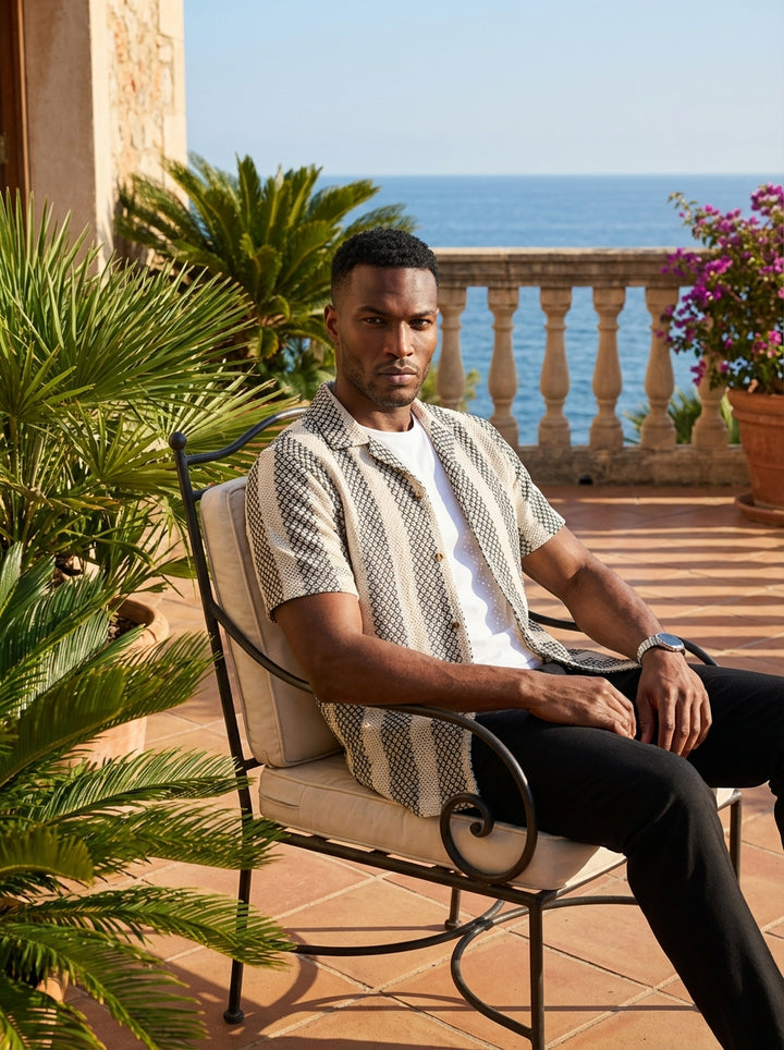 This stylish men's short-sleeve button-down features a sophisticated textured knit with bold black and off-white vertical stripes. The intricate geometric weave offers a modern, tactile finish, while the relaxed camp collar provides a contemporary edge fo