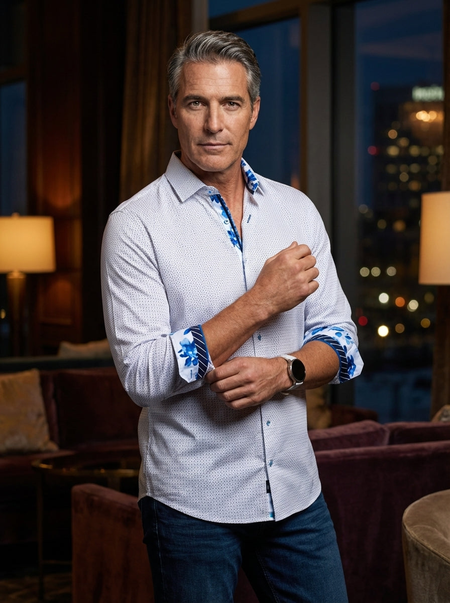 This men's white button-down shirt features a subtle navy micro-dot pattern, perfectly accented by vibrant blue floral prints on the inner collar and flipped cuffs. Tailored for a modern fit, it blends classic sophistication with bold, artistic design det