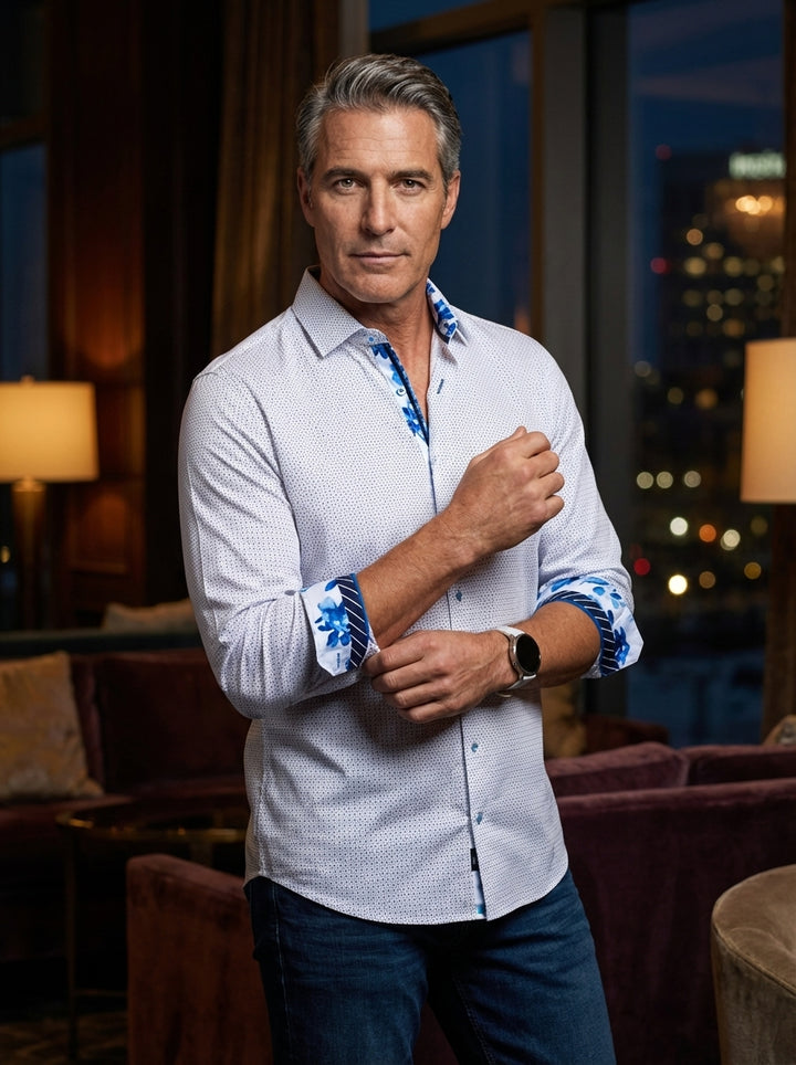This men's white button-down shirt features a subtle navy micro-dot pattern, perfectly accented by vibrant blue floral prints on the inner collar and flipped cuffs. Tailored for a modern fit, it blends classic sophistication with bold, artistic design det