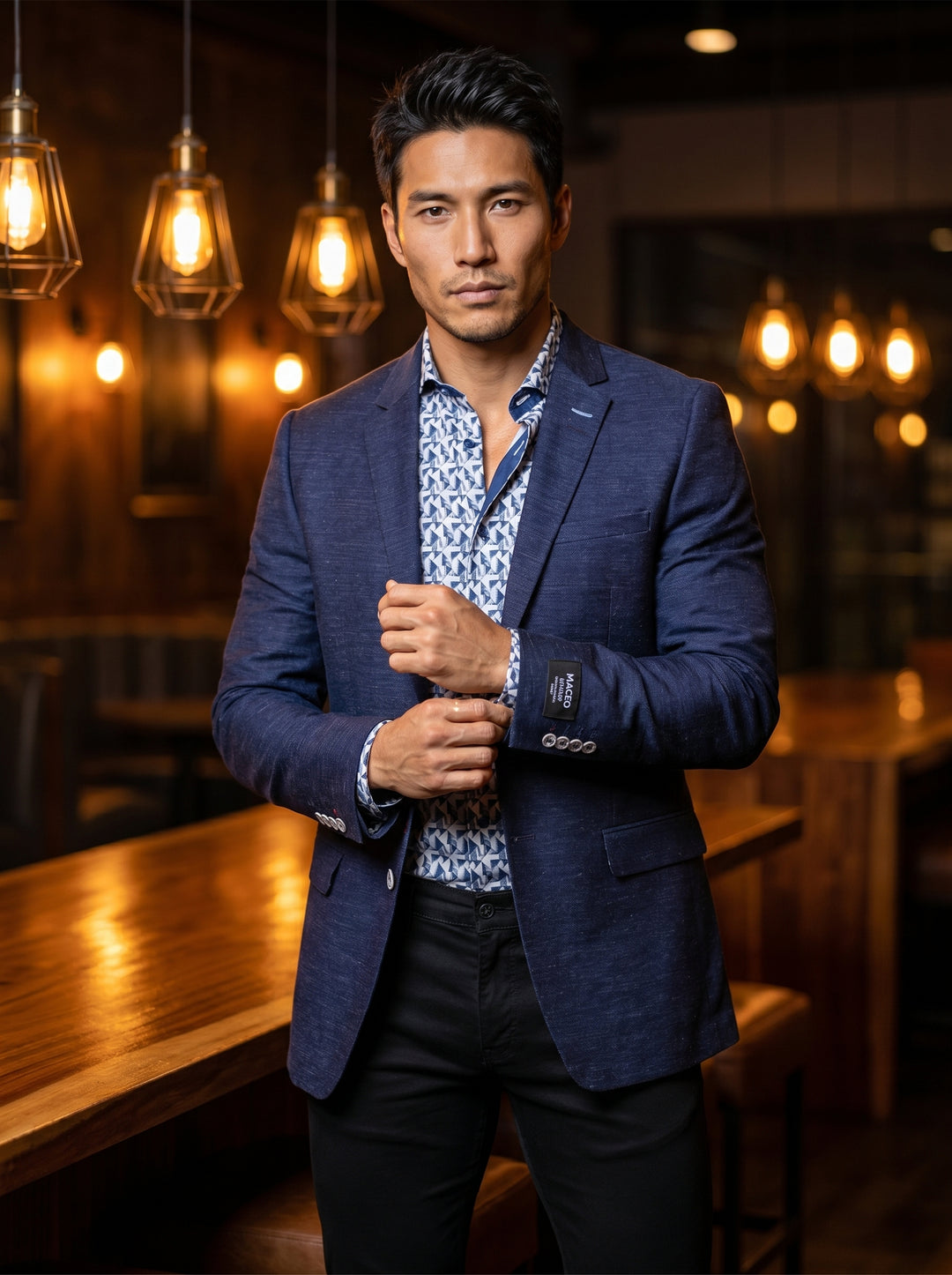 This sophisticated men's ensemble features a textured navy blue blazer with a single-breasted two-button closure and classic notched lapels. Underneath is a modern geometric print button-down shirt in shades of blue and white, paired with sleek black slim