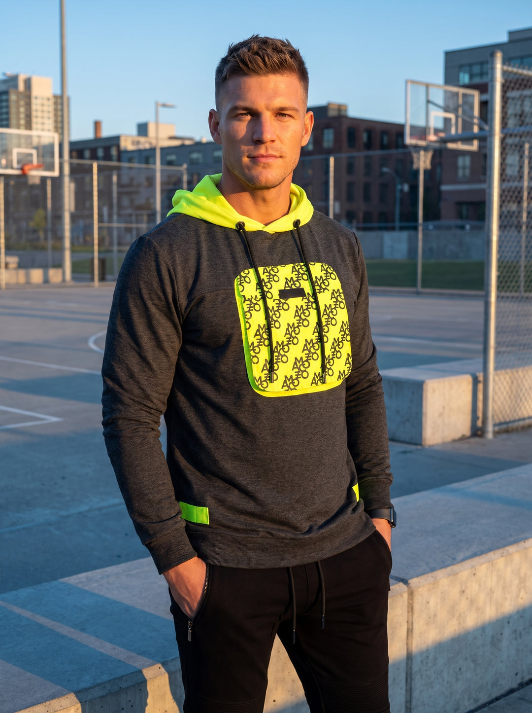 This charcoal grey heather hoodie features a vibrant neon yellow lined hood and a matching chest utility pocket with an all-over monogram print. The technical design includes drawstring adjusters and side tab accents for a high-contrast, modern streetwear