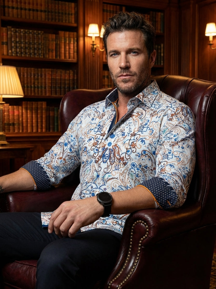 This sophisticated men's button-down features an intricate paisley and floral motif in shades of azure and bronze. It boasts unique design elements including contrasting geometric navy cuffs and trim, finished with vibrant orange piping for a modern, high