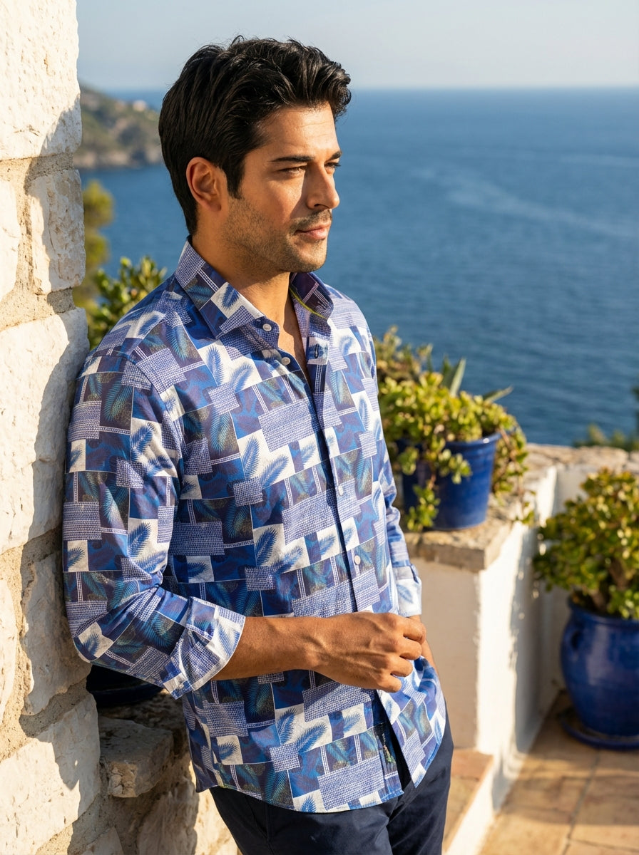 This Masutto men's button-down shirt features a vibrant blue and white patchwork design. The intricate pattern blends tropical palm fronds with geometric tiled motifs and subtle mandala accents. Crafted with a crisp collar and long sleeves, it offers mode