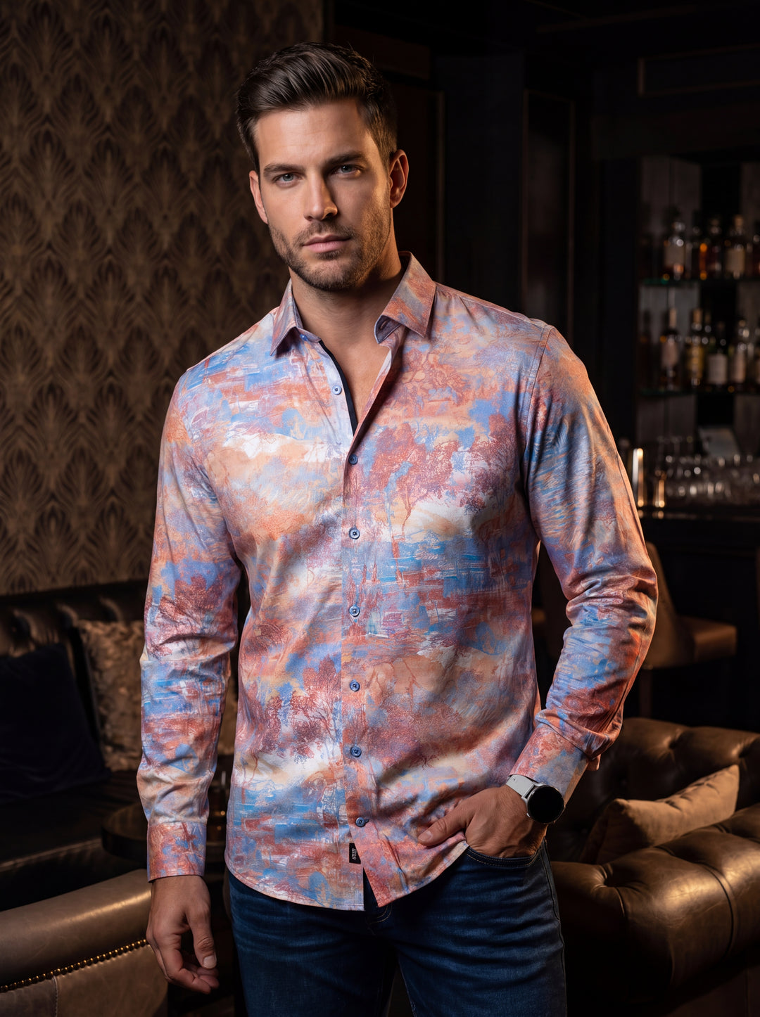A long-sleeve button-down shirt featuring an artistic, impressionistic landscape print in a vibrant palette of sunset orange, sky blue, and soft cream. The shirt includes a tailored fit, a classic collar, and contrasting dark trim along the inner placket.