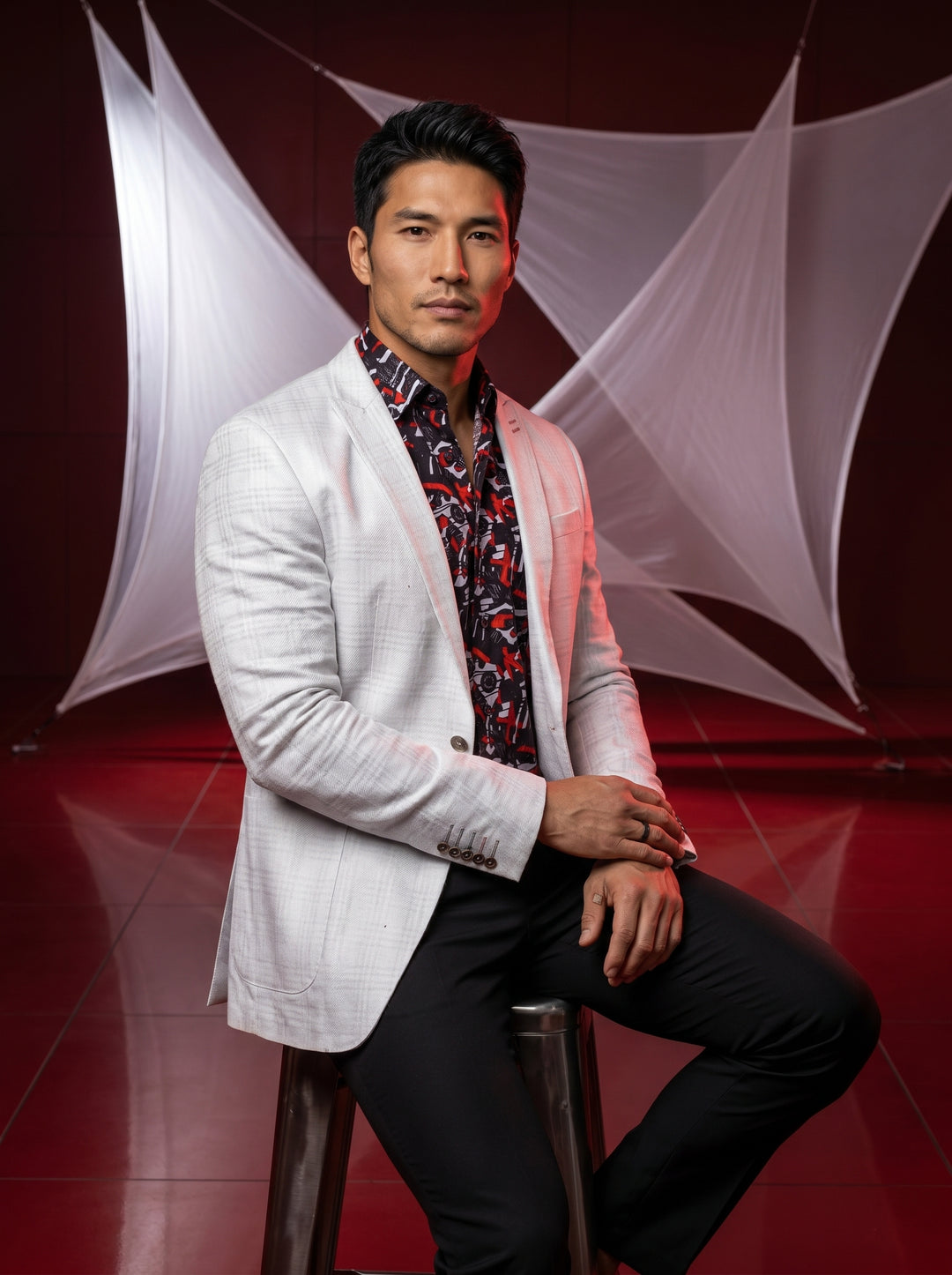 A contemporary menswear ensemble featuring a structured light grey linen-blend blazer with subtle check patterns, layered over a bold graphic print button-down shirt in black, red, and white. This sophisticated combination is paired with sleek, tailored b