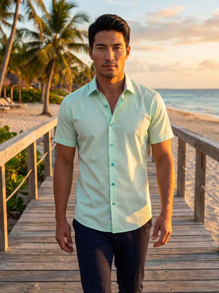 This men's short-sleeve button-down shirt features a refreshing mint green hue with a classic pointed collar. It is designed with subtle patterned inner trim and contrasting turquoise buttons, offering a modern, tailored fit that pairs perfectly with dark