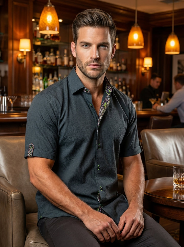 This charcoal grey, short-sleeved button-down features a subtle textured weave and vibrant lime green stitching on the buttons. The interior collar and sleeve tabs showcase a colorful patterned lining, adding a sophisticated yet playful touch to a modern 