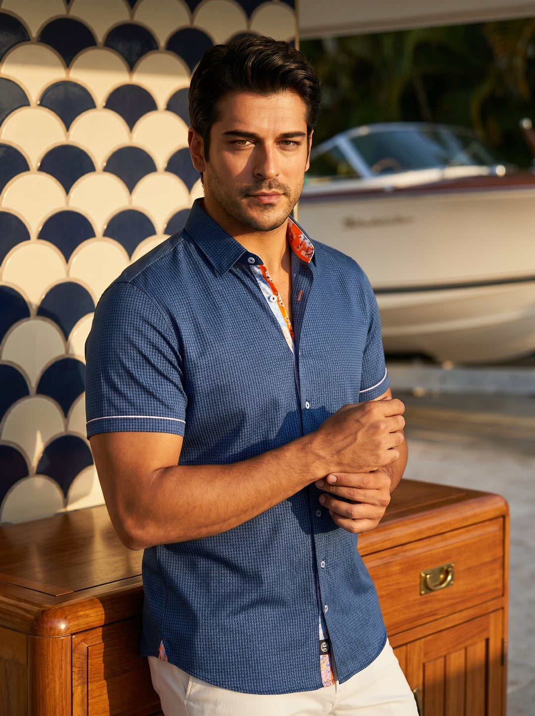 This tailored short-sleeve button-down shirt features a deep blue micro-patterned fabric with vibrant orange and white floral trim along the inner placket and collar. Finished with white contrast buttons and piping on the sleeves, it offers a sharp, moder