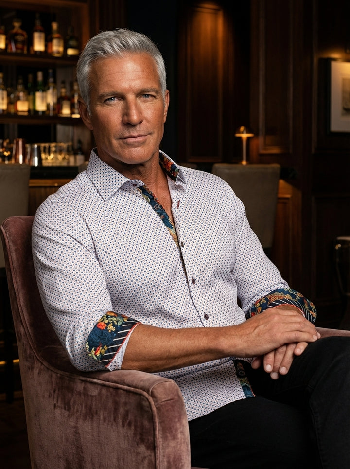 A sophisticated long-sleeve white button-down shirt featuring an intricate geometric micro-print. The design is elevated by vibrant floral and paisley contrast detailing on the inner collar and cuffs, paired with dark hardware for a modern, tailored aesth