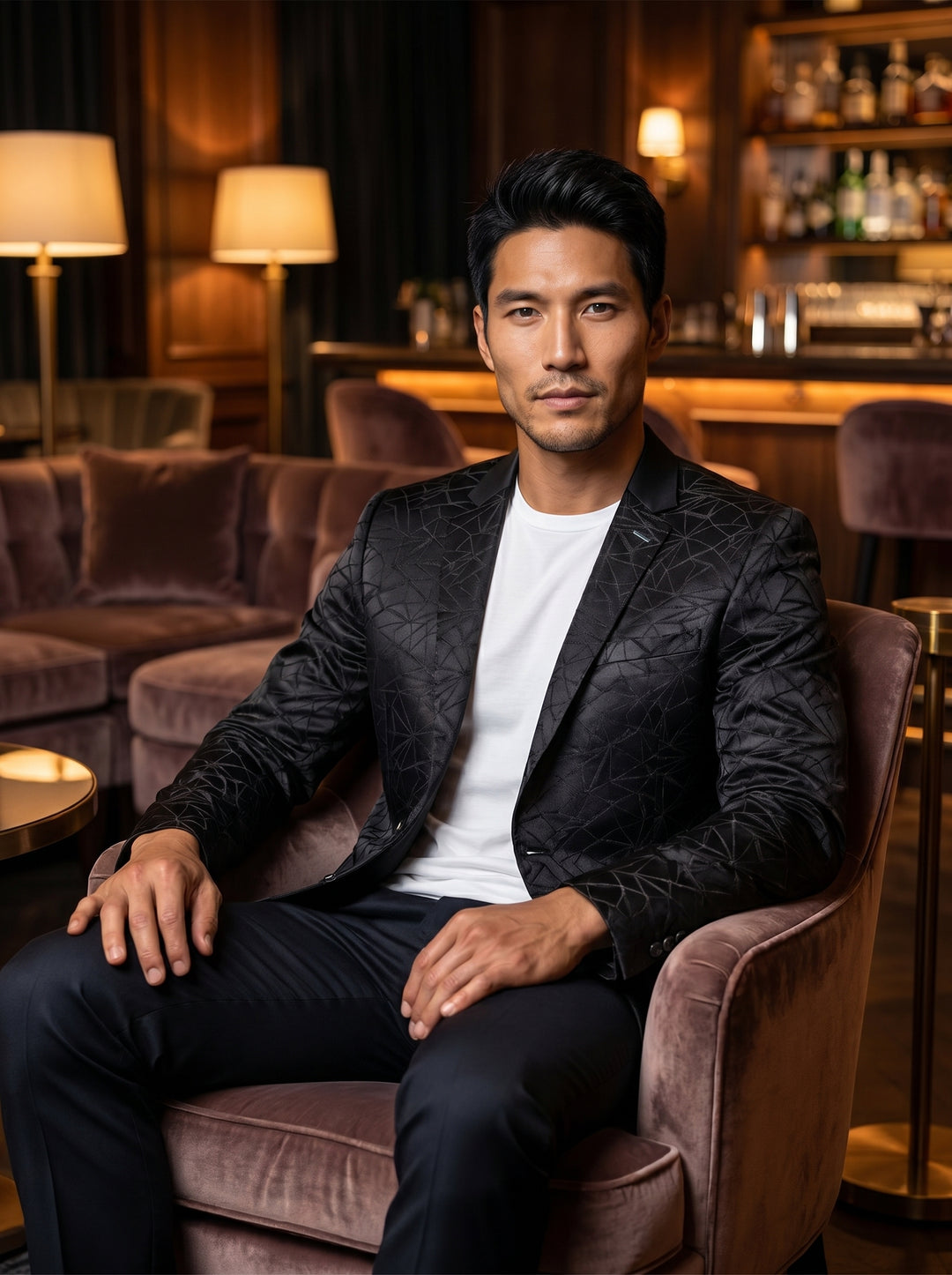 This tailored black blazer features a sophisticated satin-finish fabric with a textured, geometric jacquard pattern. It is designed with notched lapels, a single-breasted two-button closure, and functional flap pockets, offering a modern twist on classic 